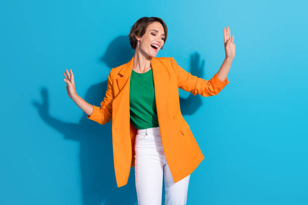 Photo of pretty handsome lady dancing carefree good mood weekend wear orange jacket white pants good mood isolated on blue color background.