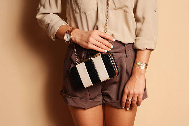 Fashionable woman with  stylish black and white clutch , accessories, watch . Elegant outfit silk blouse and  brown shorts